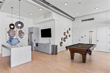 A pool table is in the middle of a room with a kitchen in the background.